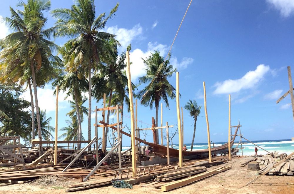 The execution of creating a traditional boat on Sulawesi Tana Biru beach surrounded by palm trees.