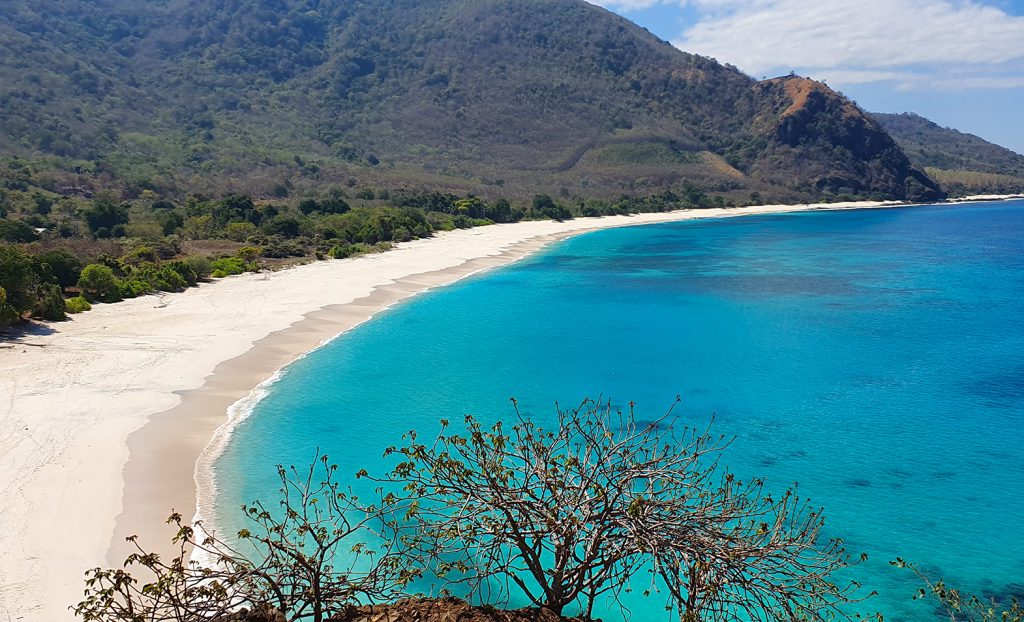 Blue beach with white sand on Alor island Indonesia surrounded by hills.